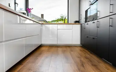 Cuisine moderne avec des armoires blanches et noires brillantes, un grand évier et un parquet au sol chaleureux.