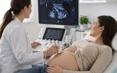 Lekarka wykonuje badanie prenatalne, przykładając głowicę USG do brzucha przyszłej mamy. Na ekranie widać obraz płodu.
