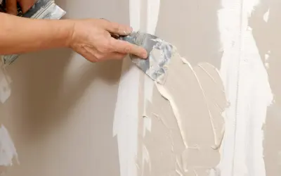 Mano stende stucco su una giuntura di cartongesso, ricordando che il cartongesso ha un verso.