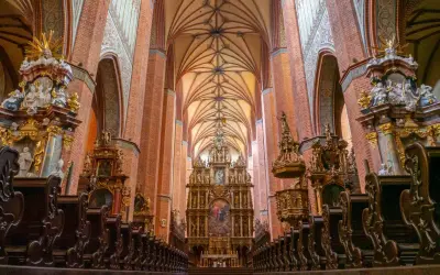 Wnętrze katedry z ceglanymi filarami, bogato zdobionym ołtarzem i rzędami drewnianych ławek. Wspaniały łęg gotyckiej architektury.