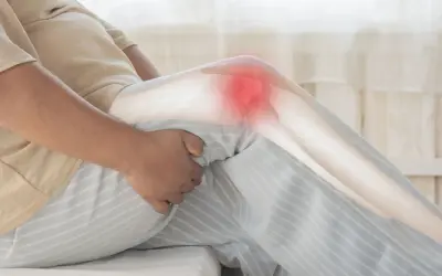 Une personne tient son genou, marqué d'une zone rouge, suggérant une douleur au genou au repos la nuit.