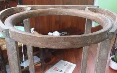 Estructura de madera de un palanganero antiguo, lista para restaurar. Se aprecian sus patas y el aro superior curvo.