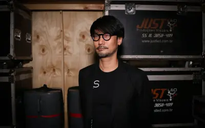 Hideo Kojima, mistrz gier wideo, w otoczeniu sprzętu, jakby przygotowywał się do kolejnej epickiej przygody.
