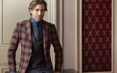 Man in a festive tartan blazer, dark blue shirt, tie, and vest. This is what holiday attire looks like.