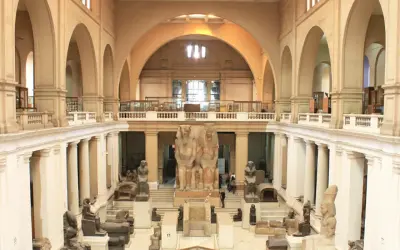 Wielka sala w muzeum w Kairze, pełna starożytnych posągów i artefaktów. Monumentalne rzeźby faraonów dominują w centrum.