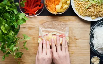 Ręce zwijają papier ryżowy z warzywami, przygotowując się do zrobienia świeżych sajgonek.