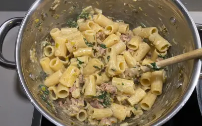 Rigatoni mit cremiger Sauce, Fenchel und Salsiccia. Ein Holzlöffel rührt die köstliche Pasta in einem Topf.
