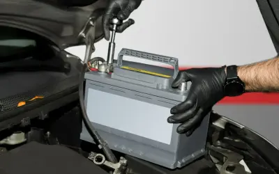 Mechanik w czarnych rękawiczkach montuje akumulator samochodowy. To kluczowy etap regeneracji akumulatora, zapewniający jego długą żywotność.