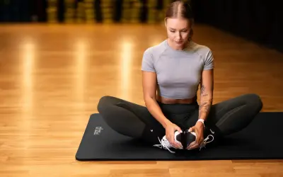 Kobieta w siłowni wykonuje ćwiczenie rozciągające na macie. Pilates co daje? Poprawia elastyczność i siłę.