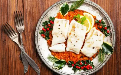 Gedünsteter Fisch auf Tomatenragout, festlich dekoriert mit Beeren und Tannenzweigen. Ein Gericht, das an italienische Weihnachtsrezepte erinnert.