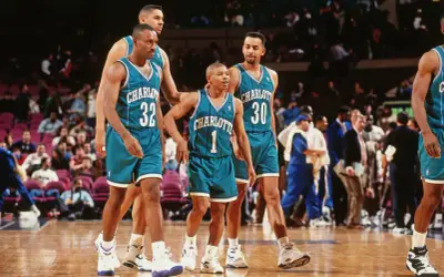 Koszykarze Charlotte Hornets, w tym najniższy koszykarz NBA, w turkusowych strojach na boisku.
