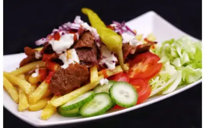En tallrik med kebab, pommes frites, tomater, gurka, sallad och en stark chili. Perfekt för dig som söker ett gott kebabsås recept.