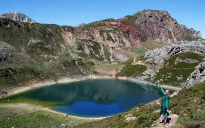 Mujer en la ladera disfruta de las vistas de un lago azul rodeado de montañas, ideal para rutas en Somiedo.