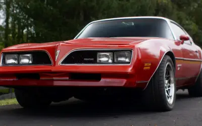 Röd Pontiac Trans Am från 70-talet, med sina karaktäristiska dubbla strålkastare och en ikonisk grill.