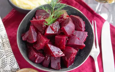 Schüssel mit gewürfelten, glänzenden roten Rüben, die man roh essen kann, garniert mit Dill. Daneben Kartoffelpüree und Besteck.