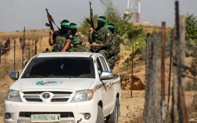 Uzbrojeni bojownicy Hamas w zielonych opaskach na głowach siedzą na białej toyocie, gotowi do akcji.