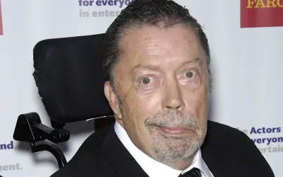 Tim Curry w wózku inwalidzkim, zmagający się z chorobą, ale wciąż z iskrą w oku.
