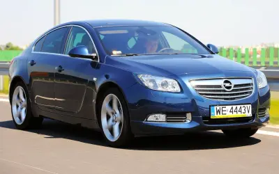 Niebieski Opel Insignia 1.6 Turbo pędzi po drodze. Kierowca wpatrzony w horyzont.