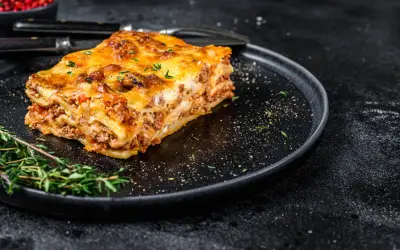 En bit gyllene lasagne på en svart tallrik, perfekt comfort food med köttfärs och ost.