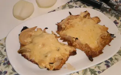 Pyszny schab w cebuli, zapieczony z serem, idealny na niedzielny obiad. Obok leżą połówki cebuli.