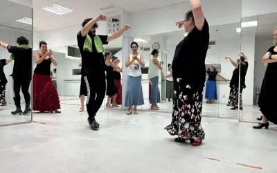 Clase de flamenco facil. Varias personas practican pasos de baile frente a espejos, con movimientos elegantes y faldas amplias.