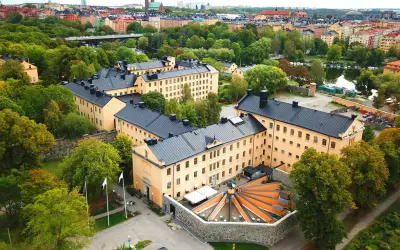 Långholmen vandrarhem, en före detta fängelsebyggnad i Stockholm, omgiven av grönskande träd och med en vacker utsikt över vattnet.