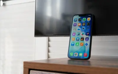 Nowy iPhone z ekranem pełnym ikon, gotowy do nagrywania rozmów. Obok czarny ekran telewizora.