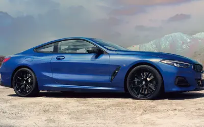 Błękitne BMW 840i z czarnymi felgami na tle pustynnego krajobrazu i gór.