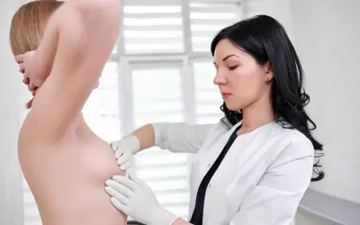 Lekarka w białym kitlu bada małe piersi pacjentki. Mammografia to ważne badanie profilaktyczne.