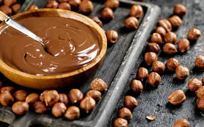 Schokocreme selber machen: Eine Schüssel voller cremiger Schokocreme neben gerösteten Haselnüssen auf einem Holzbrett.