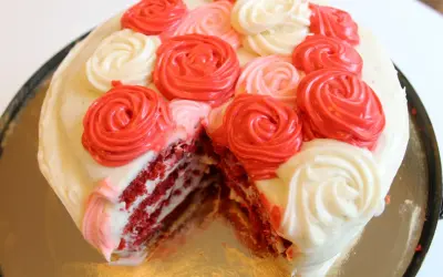En skivad red velvet cake med vit frosting och dekorationer i form av röda och rosa rosor.
