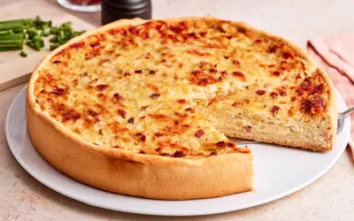 Ein goldbrauner Zwiebelkuchen mit Speck, bereit zum Servieren. Ein Stück fehlt, was Lust auf mehr macht. Perfekt für ein Zwiebelkuchen Rezept.