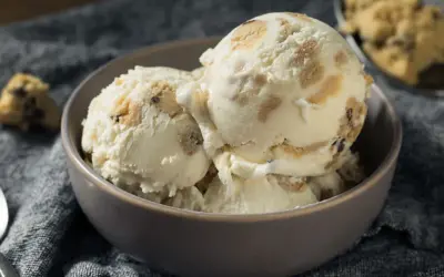 Schüssel mit cremigem Eis, durchzogen von Stückchen aus süßem Keksteig und Schokoladenstückchen. Ein Löffel liegt daneben.