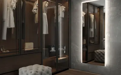 En spegel med belysning bakom spegel ger ett mjukt ljus i en lyxig walk-in-closet med kläder och accessoarer.