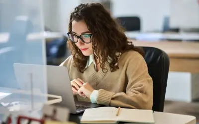 Donna con occhiali lavora al laptop, concentrata. Forse sta cercando la miglior surroga per un progetto.