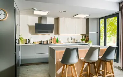 Moderna cocina con isla central, gabinetes grises y de madera, campana extractora negra y tres taburetes.