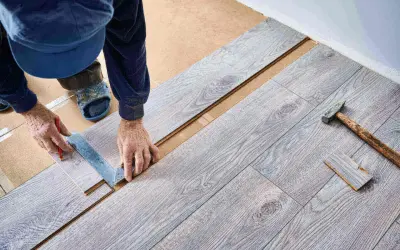 Ręce majstra mierzą i zaznaczają panel do cięcia. Układanie paneli na 1/3 postępu prac, obok leży młotek.