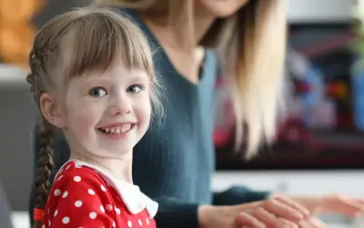 Uśmiechnięta dziewczynka w czerwonej sukience w groszki, z warkoczykami, uczy się kindersztuby od mamy.