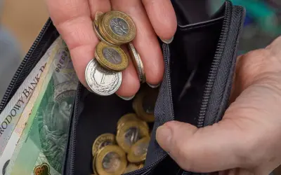 Dłoń z monetami i banknotami w portfelu. Zastanawiasz się, ile wynosi renta wojskowa?
