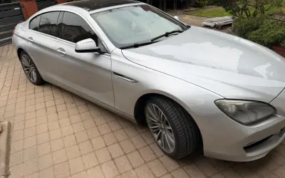 Srebrne BMW 640i z czarnym dachem stoi na podjeździe z kostki brukowej.