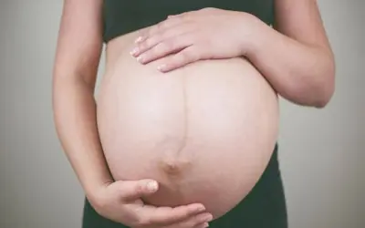 Dłońmi obejmuje ciążowy brzuch, wyczekując momentu, kiedy czuć ruchy dziecka.