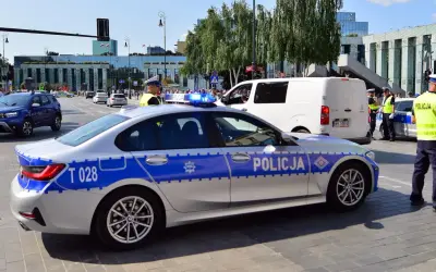 Radiowóz policyjny z włączonymi sygnałami świetlnymi na ulicy, obok policjanci.