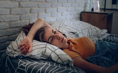 Eine Frau liegt im Bett, ihr Blick ist müde und nachdenklich. Sie kämpft mit den Symptomen eines Fatigue-Syndroms.