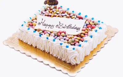 Torta rettangolare con glassa bianca, decorata con tanti smarties colorati e la scritta "Happy Birthday".