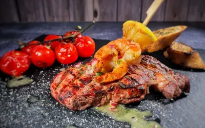 Perfektes Surf and Turf Rezept: saftiges Steak mit gegrillten Garnelen, Kirschtomaten und Zitronenspalte auf schwarzem Stein.
