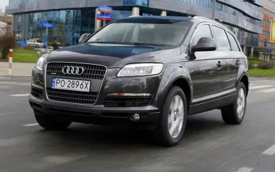 Ciemny Audi Q7 3.0 TDI w ruchu miejskim, z widocznym polskim numerem rejestracyjnym PO 2896X.