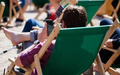 Mężczyzna w okularach przeciwsłonecznych relaksuje się na leżaku, przeglądając telefon. Idealny urlop wypoczynkowy.