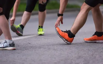 Atleti si preparano per la gara di corsa, allungando le gambe e indossando scarpe sportive colorate.