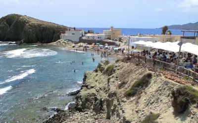 Gente disfrutando en un restaurante de Cabo de Gata, con vistas a una playa concurrida y el mar azul.