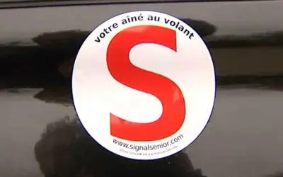 Macaron "votre aîné au volant" sur une voiture. Le S rouge est bien visible.